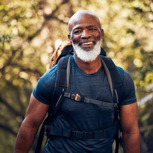 Happy, hiking and portrait of black man in forest for freedom, health and sports training. Exercise, peace and wellness with senior hiker trekking in nature for travel, summer break and adventure